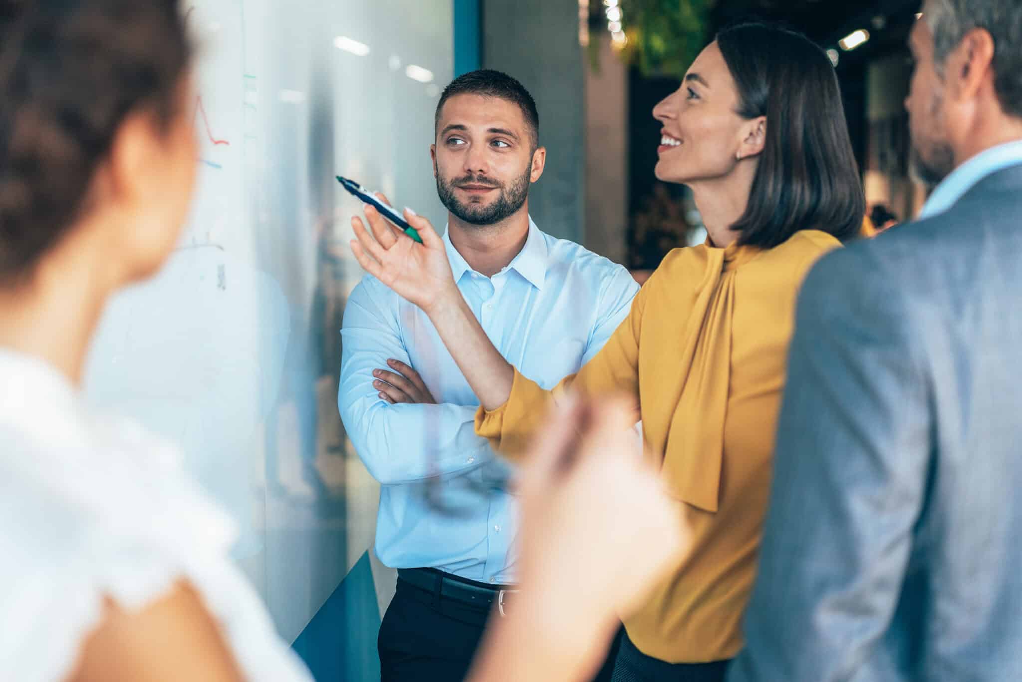 coworkers in a startup brainstorming strategies, writing a business plan on whiteboard to his team on a meeting