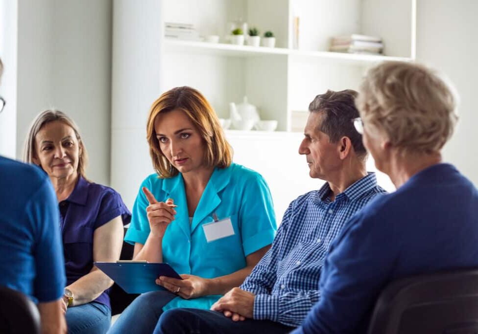 Mature nurse talking with patients during meeting in nursing home. They are discussing about mental wellbeing.