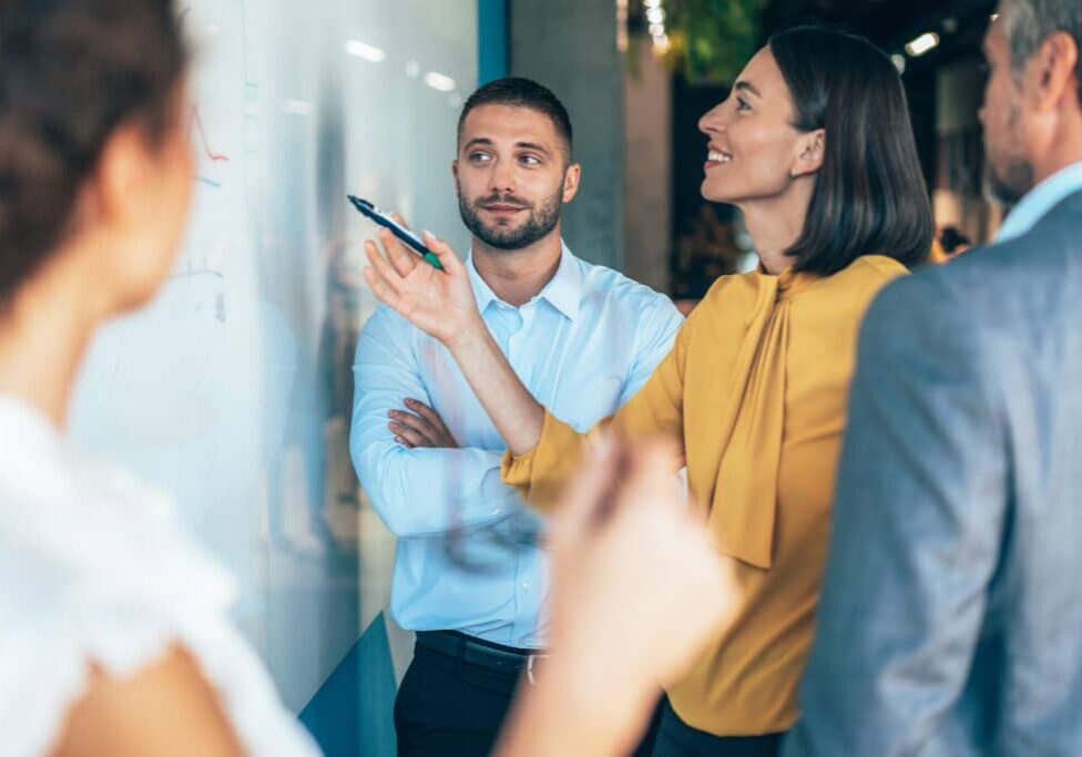 coworkers in a startup brainstorming strategies, writing a business plan on whiteboard to his team on a meeting