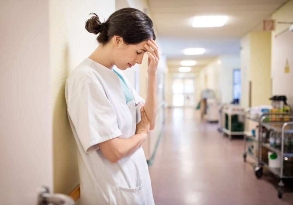 Upset female nurse standing in hospital corridor. Medical professional looking unhappy.
